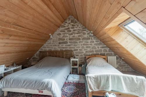 Cette chambre mansardée comprend 2 lits et un mur en pierre. dans l'établissement Maison en granite typique à Chaumeil avec cheminée, à Chaumeil