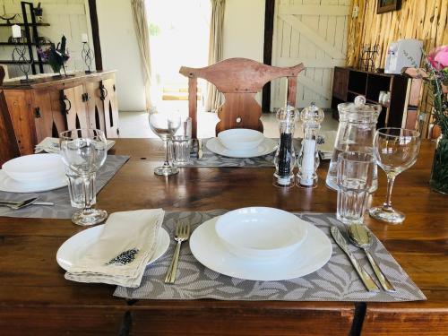 a wooden table with white plates and glasses on it at The Barn by YourHost Nanyuki Kenya in Nanyuki