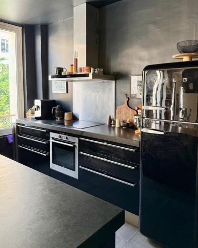 - une cuisine équipée de comptoirs noirs et d'un réfrigérateur noir dans l'établissement Spacieux et élégant appart Paris, à Paris