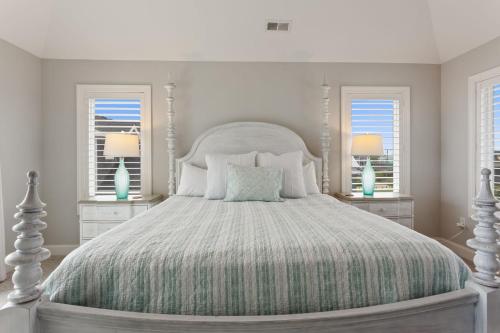 a bedroom with a white bed with two windows at 3025 - Who's On First in Southern Shores