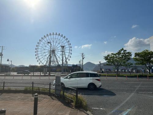 a white car parked in a parking lot with a ferris wheel at Guest House" Ro" takezaki in Amanogōchō