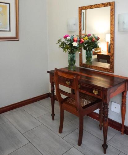 a wooden table with a mirror and flowers on it at Coach House Hotel & Spa Tzaneen in Tzaneen