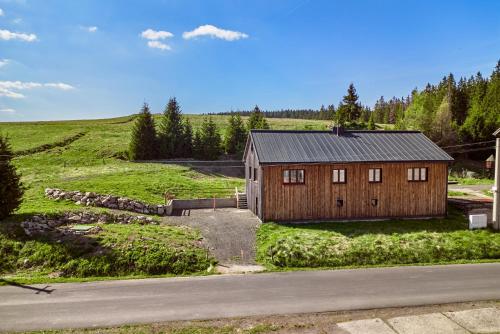 a wooden house in a field next to a road at Apartmány Jelení vrch in Nové Hamry