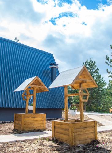 two wooden gazebos in front of a blue building at Natural Dream Blidinje in Rudo Polje