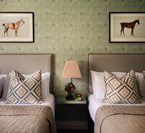 two beds in a hotel room with paintings of horses on the wall at Horse & Jockey Hotel in Horse and Jockey
