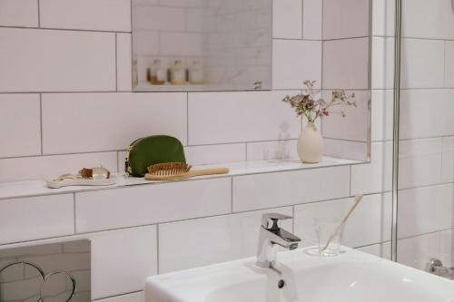 a white tiled bathroom with a sink and a vase of flowers at Thistle Suites Royal Garden in Edinburgh