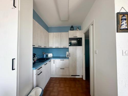 Elle comprend une petite cuisine avec des placards blancs et des murs bleus. dans l'établissement Emplacement idéal à Port Camargue, au Grau-du-Roi