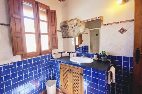 La salle de bains est pourvue de carrelage bleu, d'un lavabo et d'un miroir. dans l'établissement Casitas La Cueva, à Guájar-Faragüit