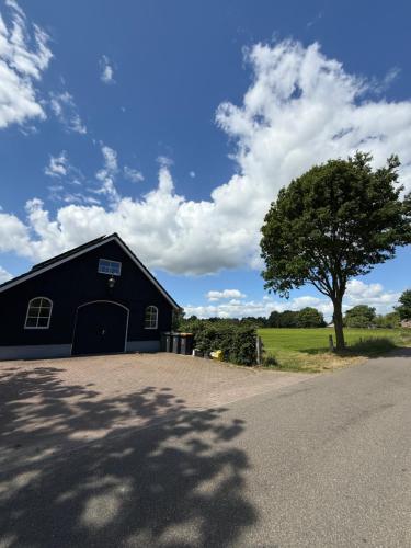 a black barn with a tree in a field at Gastenverblijf met jaccuzi in Keijenborg