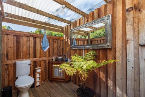 a bathroom with a toilet and a mirror on a wooden wall at Zen Valley Glamping in Plettenberg Bay