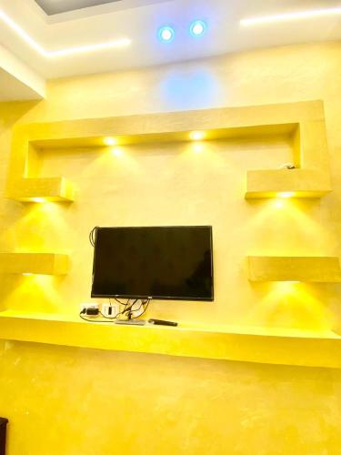 a tv on a yellow wall with shelves at sphinx one centre hotel in Banī Ghālib