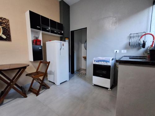 a kitchen with a white refrigerator and a table and chair at Kitnet Completa perto da Praia e do Centro, Roupas de Cama e Banho in Ilha Comprida