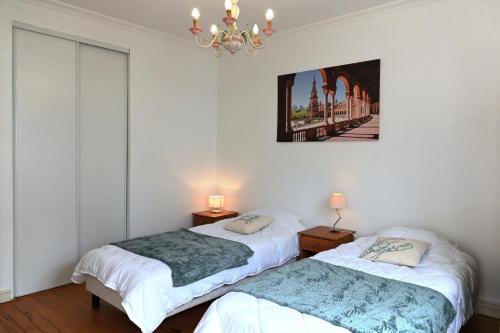 two beds in a room with white walls and a chandelier at La Pause Royannaise - 500 m de la plage in Royan