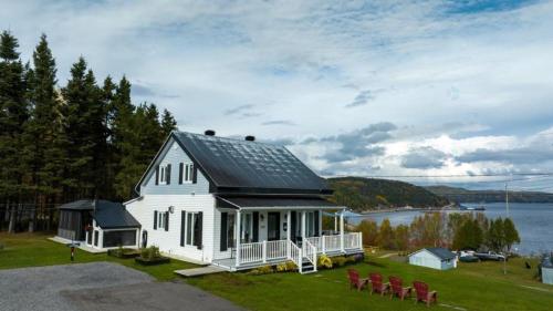 a white house with a black roof and chairs at Les chalets de la colline inc in Baie-Sainte-Catherine