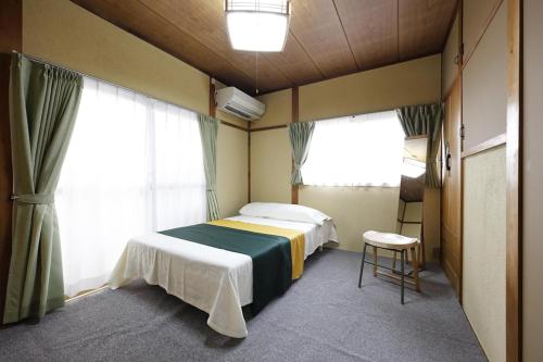 a bedroom with a bed and two windows and a stool at うぬまの森かんとりー in Kakamigahara