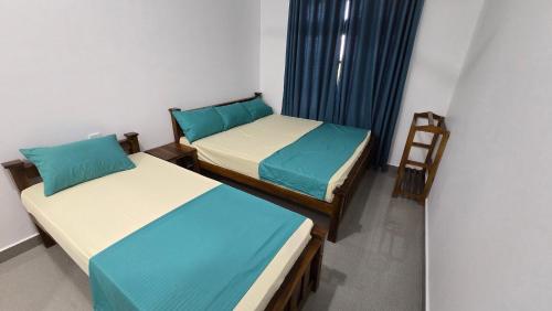 two beds in a small room with blue curtains at Ramiy Resort Batticaloa in Batticaloa