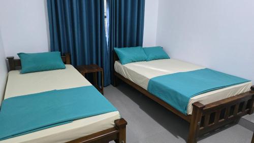 two twin beds in a room with blue curtains at Ramiy Resort Batticaloa in Batticaloa
