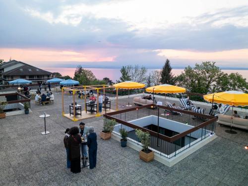 a group of people standing around a patio with umbrellas at Côté Lac Hostel Evian in Évian-les-Bains