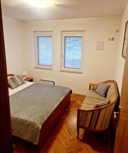 a bedroom with a bed and a chair and two windows at Drive & Stay Korčula in Korčula