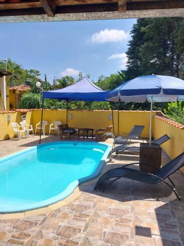 a swimming pool with chairs and an umbrella at Chácara Catavilela in Jacareí
