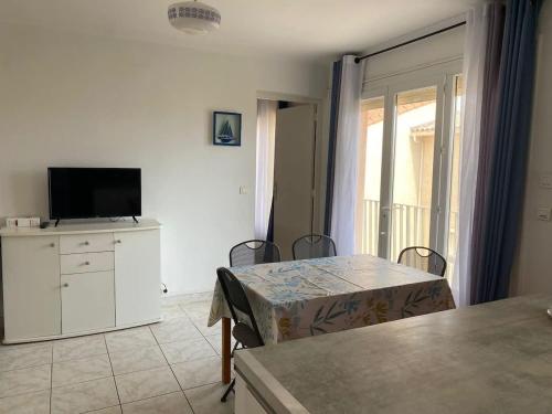 un salon avec une télévision et une table avec des chaises dans l'établissement Appartement au centre-ville - Proche de la plage, à Valras-Plage