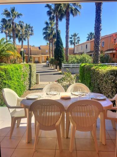 une table et des chaises en bois sur une terrasse avec des palmiers dans l'établissement Pavillon pour 4 personnes dans une résidence avec piscine, à Valras-Plage