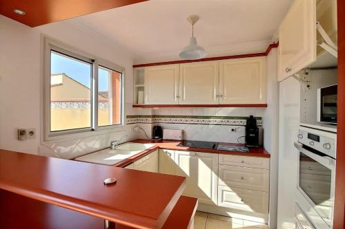 une cuisine avec des armoires blanches, un évier et une fenêtre dans l'établissement Spacieuse maison pour 6 personnes, proche mer et commerces, à Valras-Plage