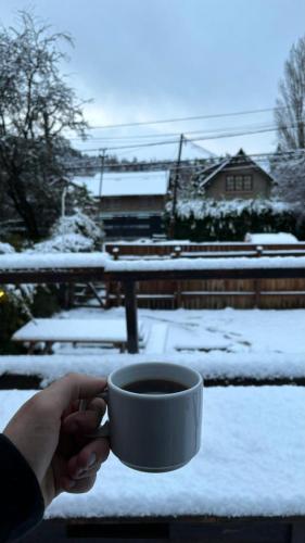 a person holding a cup of coffee in the snow at Alaska Patagonia Hostel in San Carlos de Bariloche