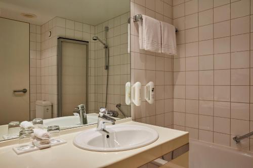 a bathroom with a sink and a mirror and a tub at H+ Hotel Leipzig-Halle in Landsberg OT Peißen