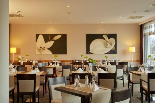 a dining room with tables and chairs and paintings on the walls at H+ Hotel Leipzig-Halle in Landsberg OT Peißen