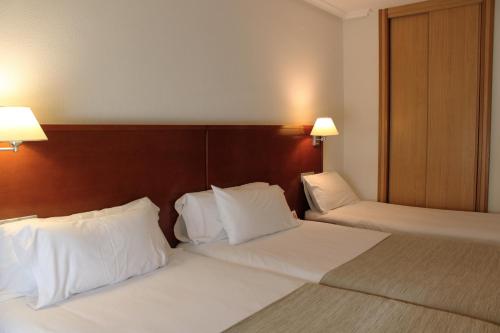 two beds in a hotel room with white pillows at México PR in Santiago de Compostela