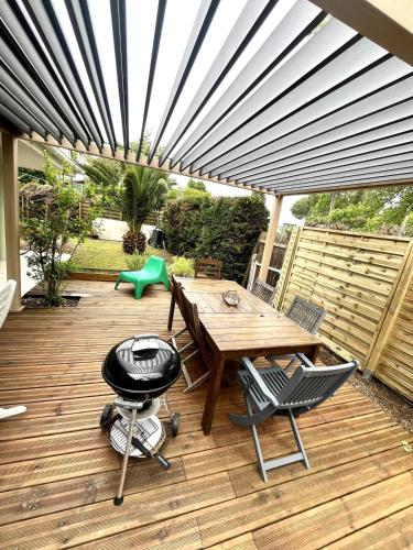 a patio with a wooden table and chairs and a grill at Surf, Skate, Golf house Seignosse in Seignosse