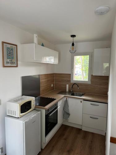 une petite cuisine avec des armoires blanches et un micro-ondes dans l'établissement Maison chaleureuse bassin Arcachon, à La Celle-sous-Gouzon