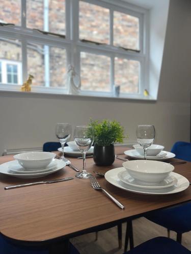 a wooden table with plates and wine glasses on it at The Lucia Apartments I - 2 Bedroom Town Centre Apartment - Contractor Friendly - Free Parking - Full Kitchen - Washer Dryer - Spacious - Ideal for Work Stays in Huntingdon