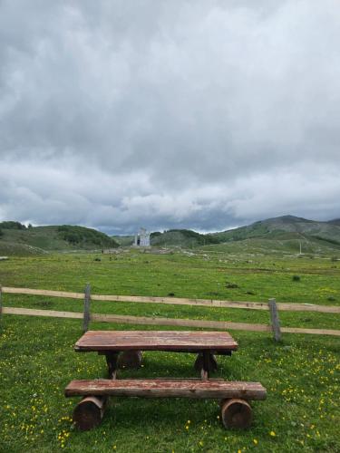 a wooden picnic table in a field with a fence at Guest House Ethno Village Milogora in Pluzine
