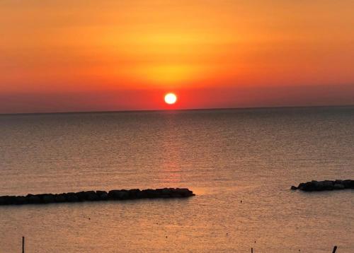 a sunset over the ocean with rocks in the water at Apartment Sunrise Pesaro in Pesaro