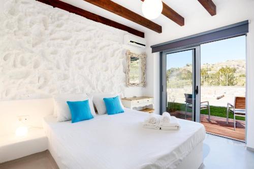 a white bedroom with a large bed with blue pillows at Villa Dione Seastone by Villa Plus in Kiotari