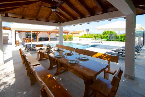 a wooden table and chairs under a pavilion with a pool at Vacation villa Matic with 7 bedrooms in Sinj