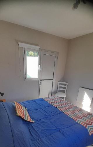 a bedroom with a blue bed with a window and a chair at la posta in Puerto Pirámides