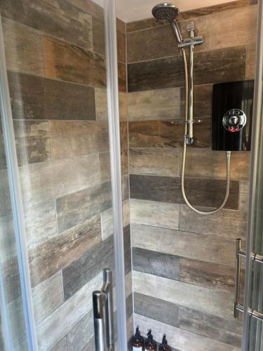 a bathroom with a shower with a wooden wall at The Corner Cottage in Wotton-under-Edge
