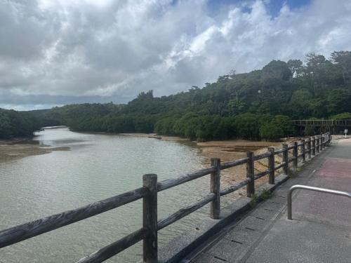 a river with a wooden fence next to a bridge at 満天の星空に出会える宿 やんばるtgコテージ in Ujimi