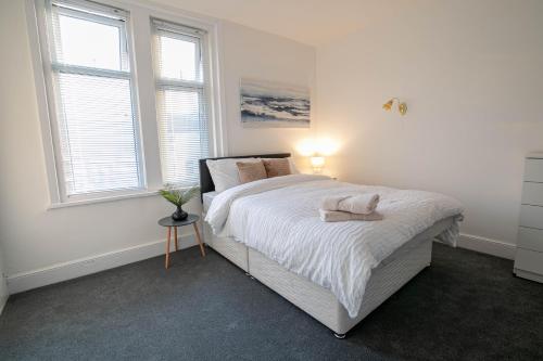 a bedroom with a bed with white sheets and two windows at 3 Bed Stylish & Spacious Home, Sleep up to 7ppl in Portsmouth