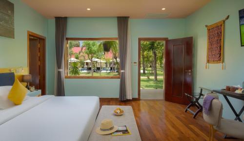 a bedroom with a bed and a table and a window at Sala Siem Reap Resort in Siem Reap