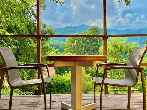 a table and two chairs on a deck with a view at Chalé com lareira pertinho de Monte Verde in Camanducaia