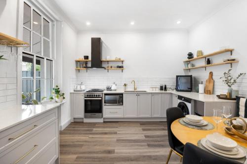 a kitchen with white cabinets and a table with a dining room at Velvet Cottage - Couple's City Escape with Courtyard in Adelaide