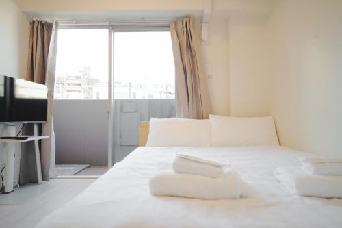 a bedroom with a bed with white sheets and a window at Cu Tennoji in Osaka