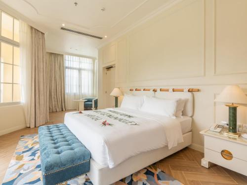 a bedroom with a large white bed with a blue bench at Legend Valley Hotel Ha Nam in Phủ Lý