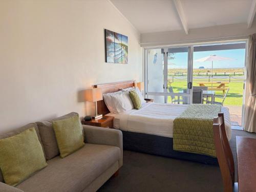 a bedroom with a bed and a couch and a window at Baileys At The Beach in Whitianga