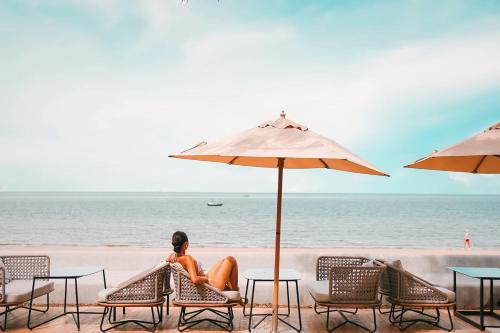 a woman sitting on the beach under an umbrella at Kundala Beach Resort Hua Hin in Hua Hin