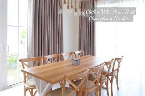 a dining room table with wooden chairs and a chandelier at Chillin Villa Novaworld Phan Thiet in Bình Tú